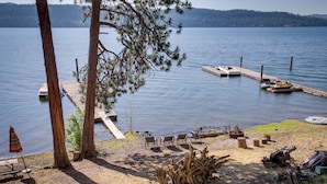 A lakeside dock with boats, a picnic table, and chairs. - Lakefront Bliss: Coeur D'alene Cabin w/ Dock! (Coeur d'Alene)