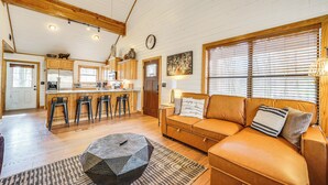A spacious living room with a leather sofa, a coffee table, and a kitchen area with wooden cabinets and a bar.