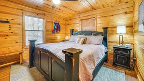 A wooden cabin bedroom with a bed, nightstand, and a ceiling fan.