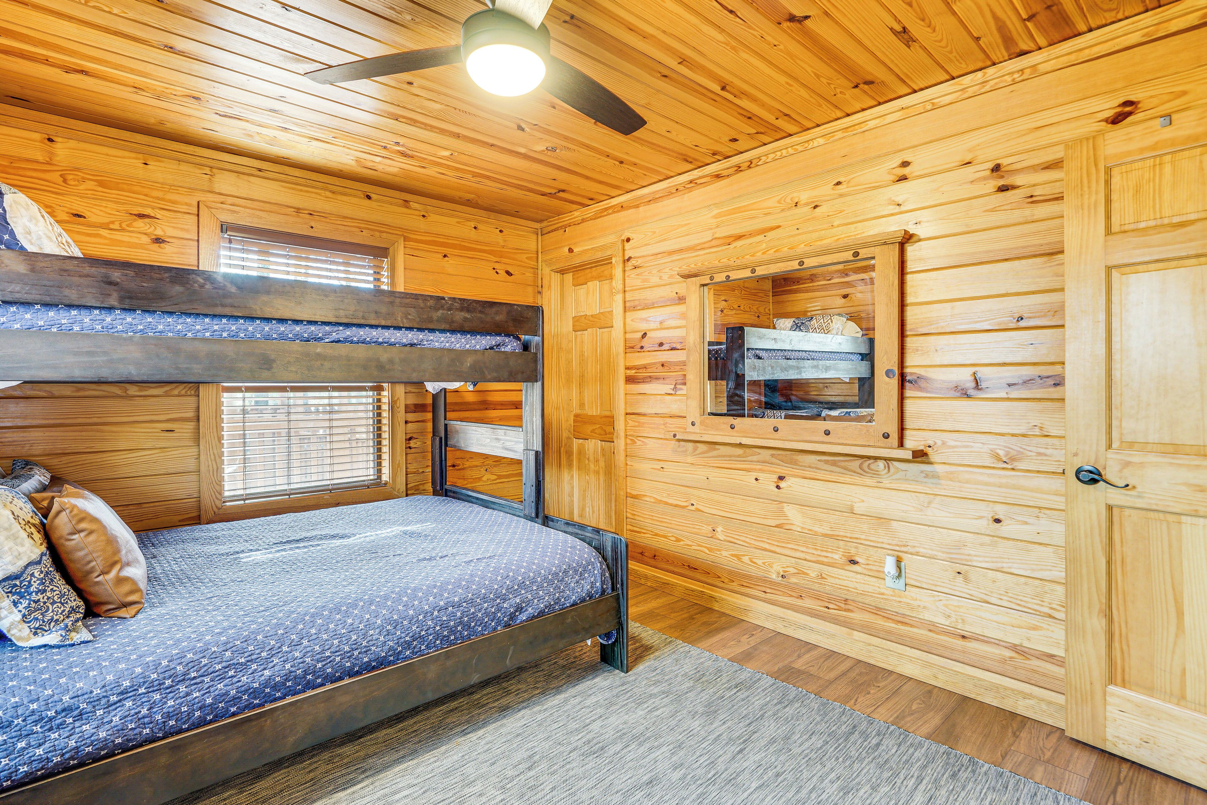 A bunk bed with a blue mattress and pillows, wooden walls, a window with blinds, and a ceiling fan.