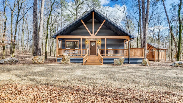 A log cabin with a wooden porch and a front door, surrounded by trees.