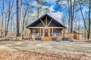 Une cabane en rondins avec un porche en bois et une porte d’entrée, entourée d’arbres.