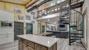 A spacious kitchen with a central island, a dining area with a sofa, and a spiral staircase leading to an upper level. - Family-friendly Broken Bow Home w/ Deck & Grill! (Broken Bow)