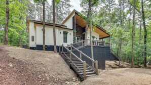 A cabin with a wooden staircase leading to a deck, surrounded by trees. - Family-friendly Broken Bow Home w/ Deck & Grill! (Broken Bow)