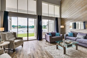 Een ruime woonkamer met een grote schuifpui naar een balkon, ingericht met een bank, fauteuils en een glazen salontafel.