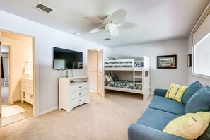 A bedroom with a bunk bed, a white dresser, a blue sofa, and a ceiling fan.