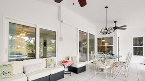 Un vaste patio comprenant une table et des chaises, un canapé avec des coussins et un ventilateur de plafond.