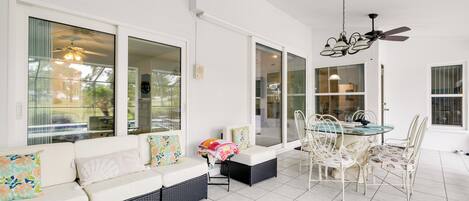 A spacious patio area with a dining table and chairs, a sofa with cushions, and a ceiling fan.