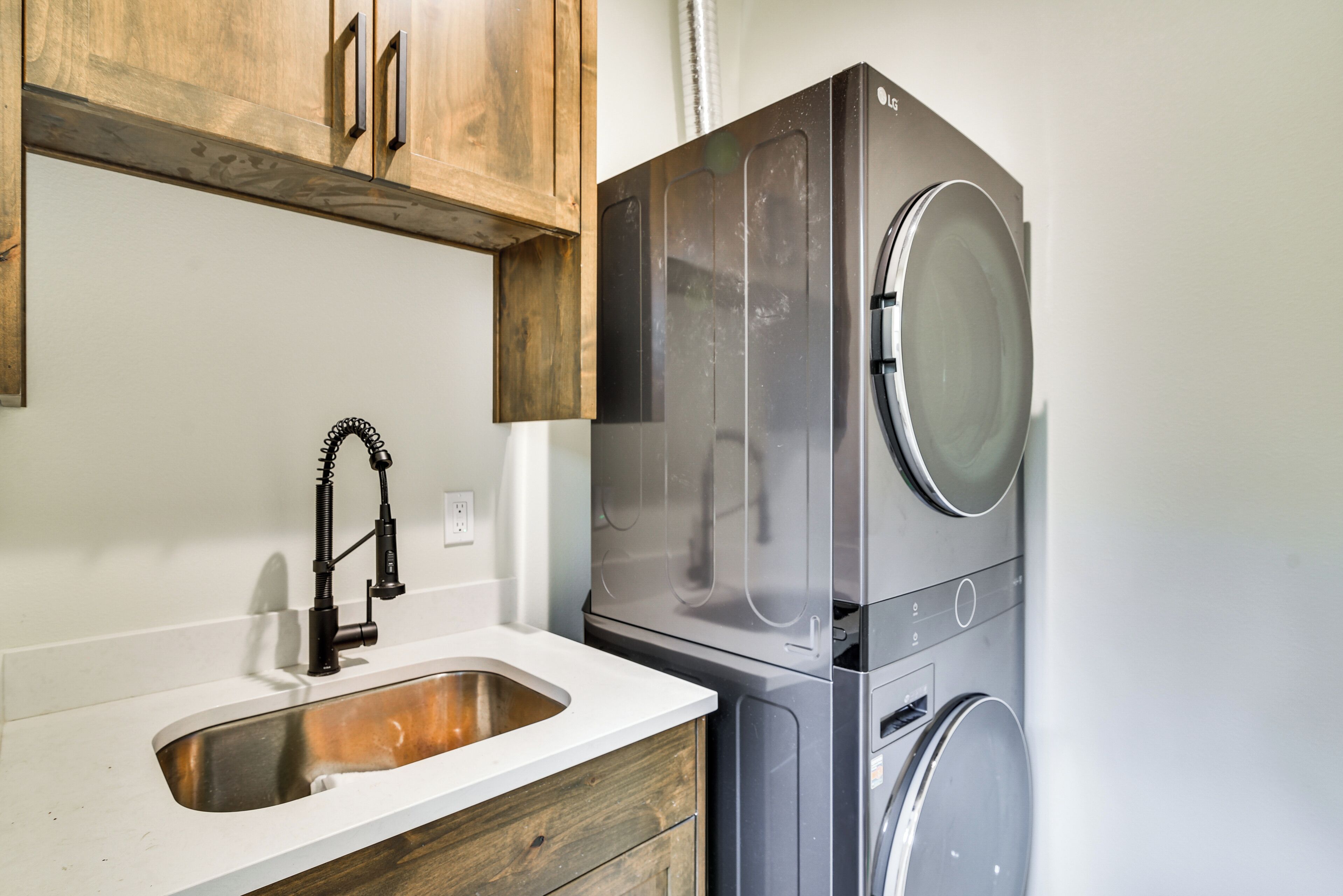 Une cuisine compacte dotée d’un évier en acier inoxydable, de meubles en bois et d’un lave-linge et d’un sèche-linge modernes intégrés.