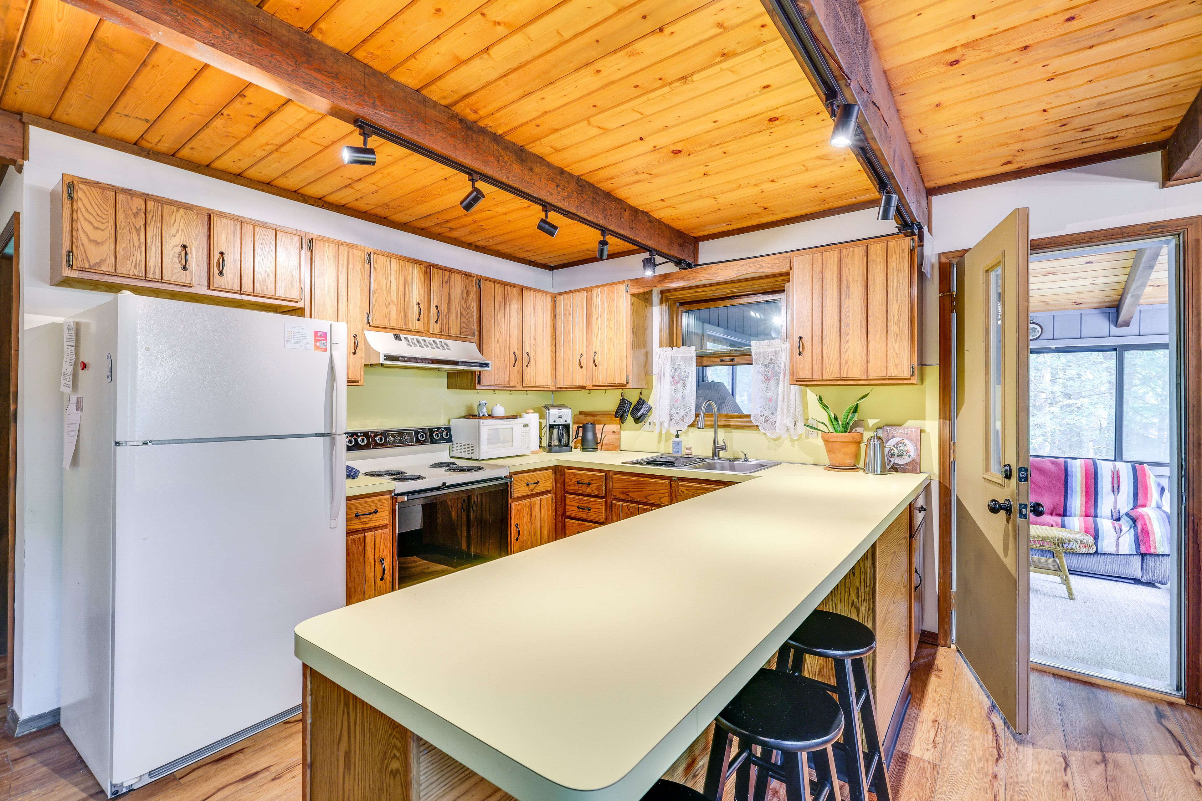 A kitchen with wooden cabinets, a white refrigerator, a large island, and a window overlooking a balcony.