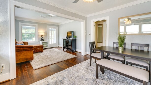 A spacious living room with hardwood flooring, a large white rug, a brown sofa, and a dining area with a wooden table and benches. - Pet-friendly Home w/ Yard, Near Downtown Royal Oak (Royal Oak)