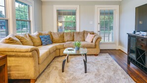 A living room with a beige sectional sofa, a glass coffee table, and a TV stand. - Pet-friendly Home w/ Yard, Near Downtown Royal Oak (Royal Oak)