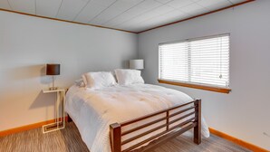 A bedroom with a bed, a bedside table with a lamp, a window with blinds, and a ceiling light. - Stillwater Home - Walk to Boone Pickens Stadium! (Stillwater)