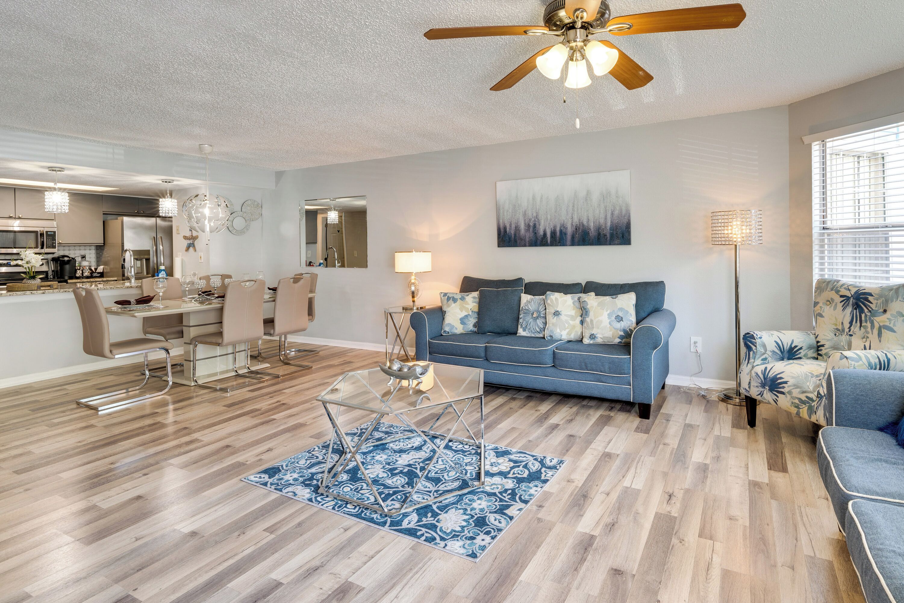 A modern living room with a blue sofa, a coffee table, and a dining area with a glass table and chairs.