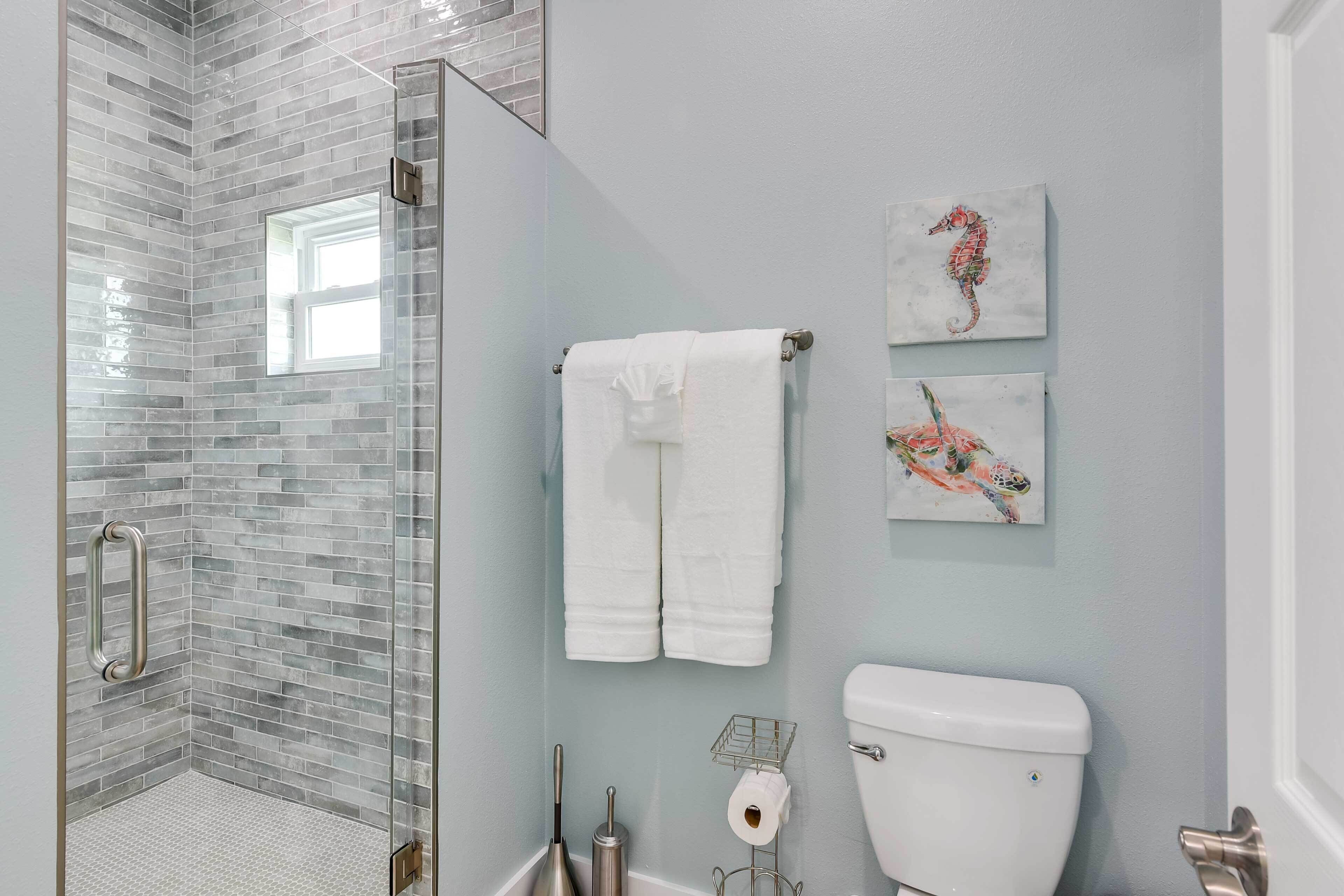 Een badkamer met een glazen douche, een wit toilet en twee handdoeken aan een rek.