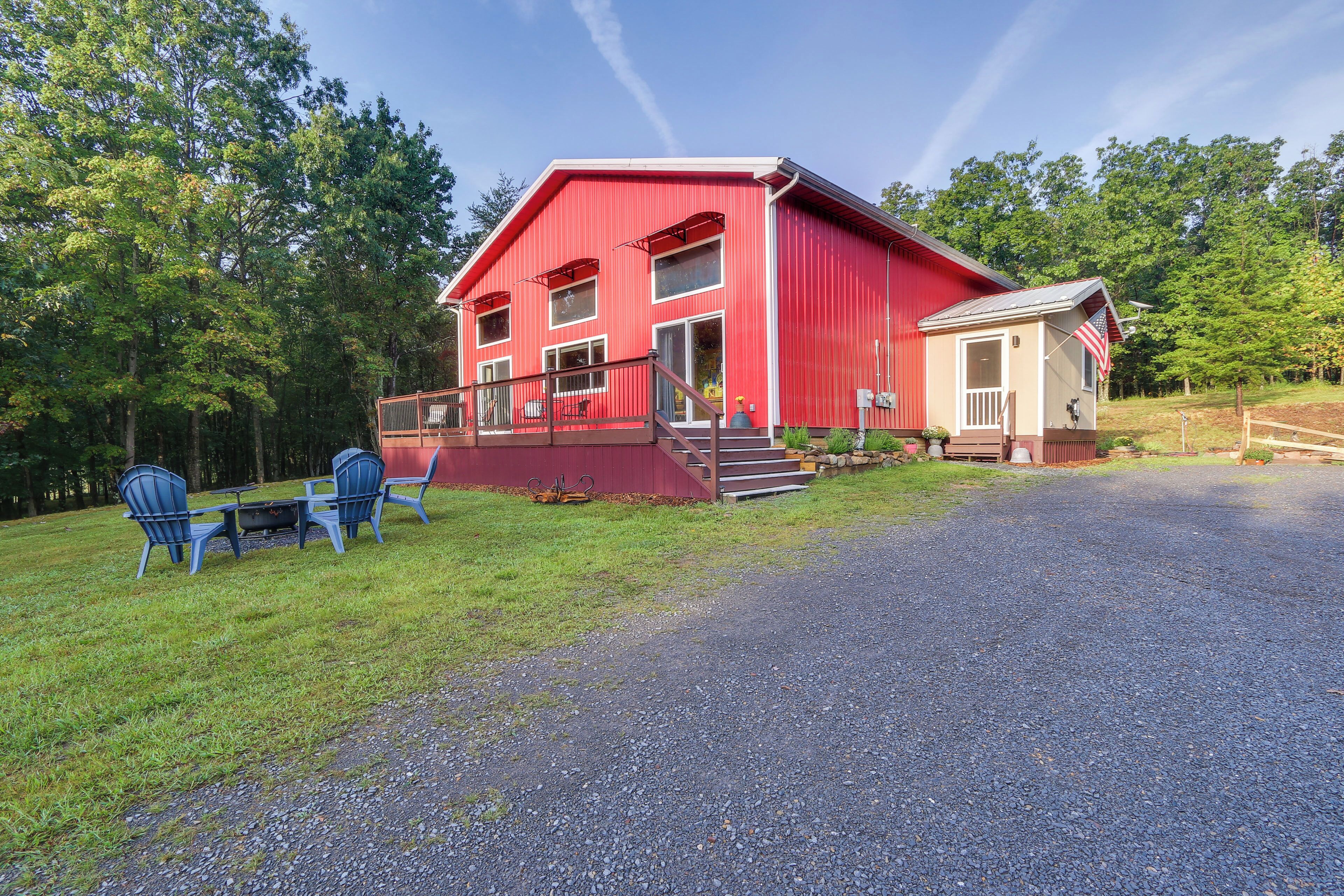 A red barn with a porch, a small attached structure, and a gravel driveway.