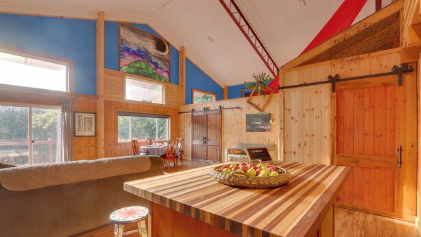 Una cucina con mobili in legno, un'isola grande con un cesto di frutta e vista all'esterno attraverso ampie finestre.