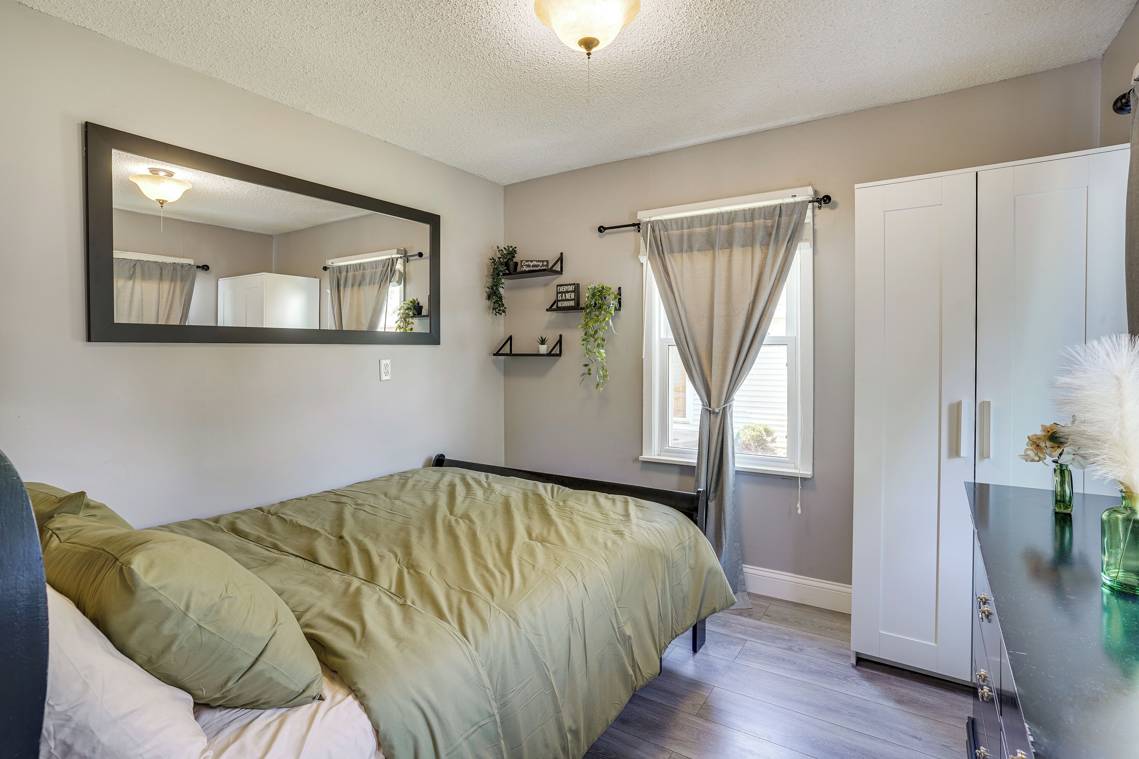 A bedroom with a bed, a wardrobe, a mirror, and a window with curtains.