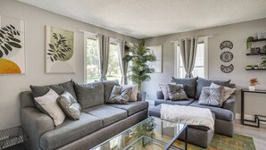 Ein modernes Wohnzimmer mit grauen Sofas, einem Glastisch und dekorativen Wandbildern.