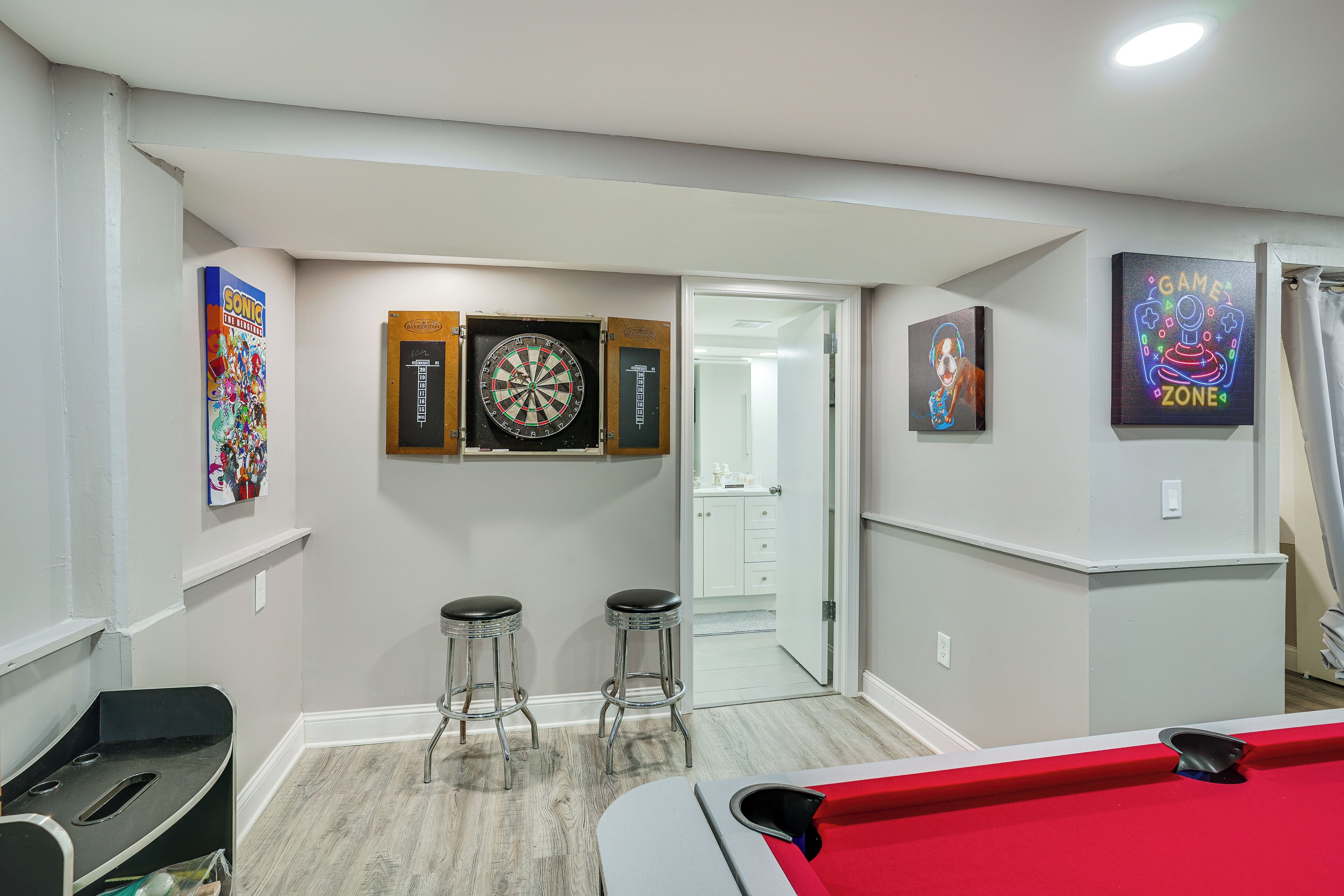 A room with a dartboard, two stools, a pool table, and artwork on the walls.