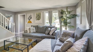 Ein Wohnzimmer mit grauem Sofa, einem Glastisch und einer großen Pflanze.