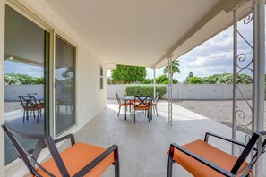 A covered patio with a table and chairs, a view of the surrounding greenery, and a white wall with a window. - Sun City Retreat w/ Patio Near Golfing & Hiking! (Sun City)