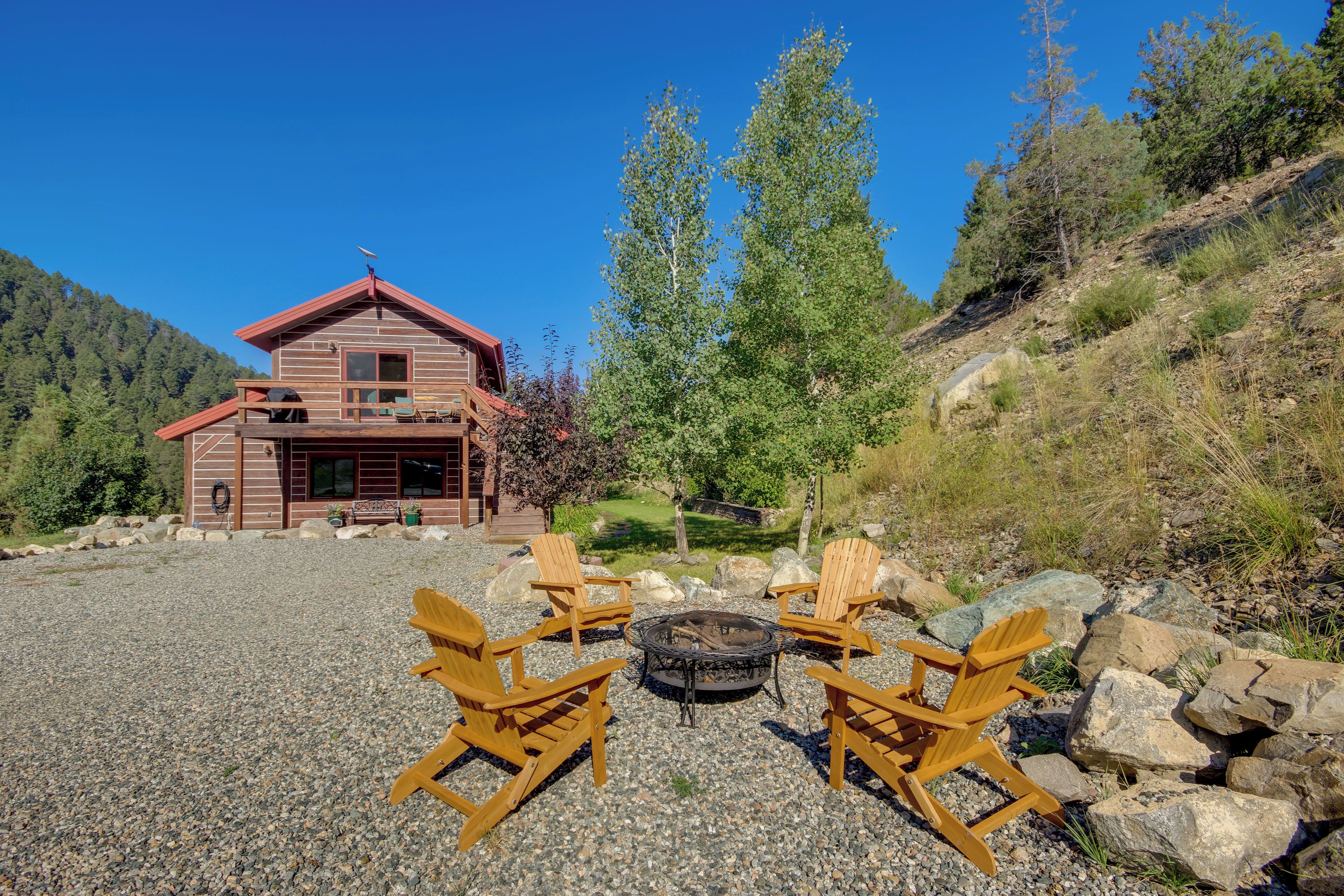 A wooden cabin with a fire pit and four Adirondack chairs in front.