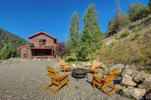 A wooden cabin with a fire pit and four Adirondack chairs in front.
