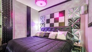Um quarto moderno com uma cama grande, um painel decorativo na parede e uma mesa de cabeceira com uma luminária.