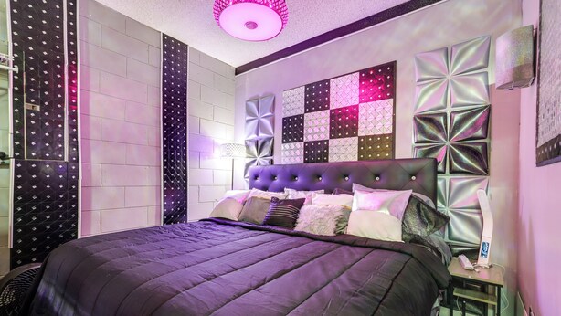 Une chambre à coucher moderne avec un grand lit, un panneau mural décoratif et une table de chevet avec une lampe.