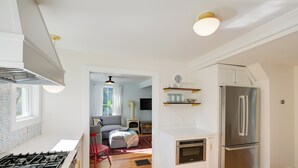 Une cuisine moderne équipée d’une cuisinière à gaz, d’un four et d’un réfrigérateur en acier inoxydable. On y trouve également un coin repas avec une chaise rouge et un canapé.