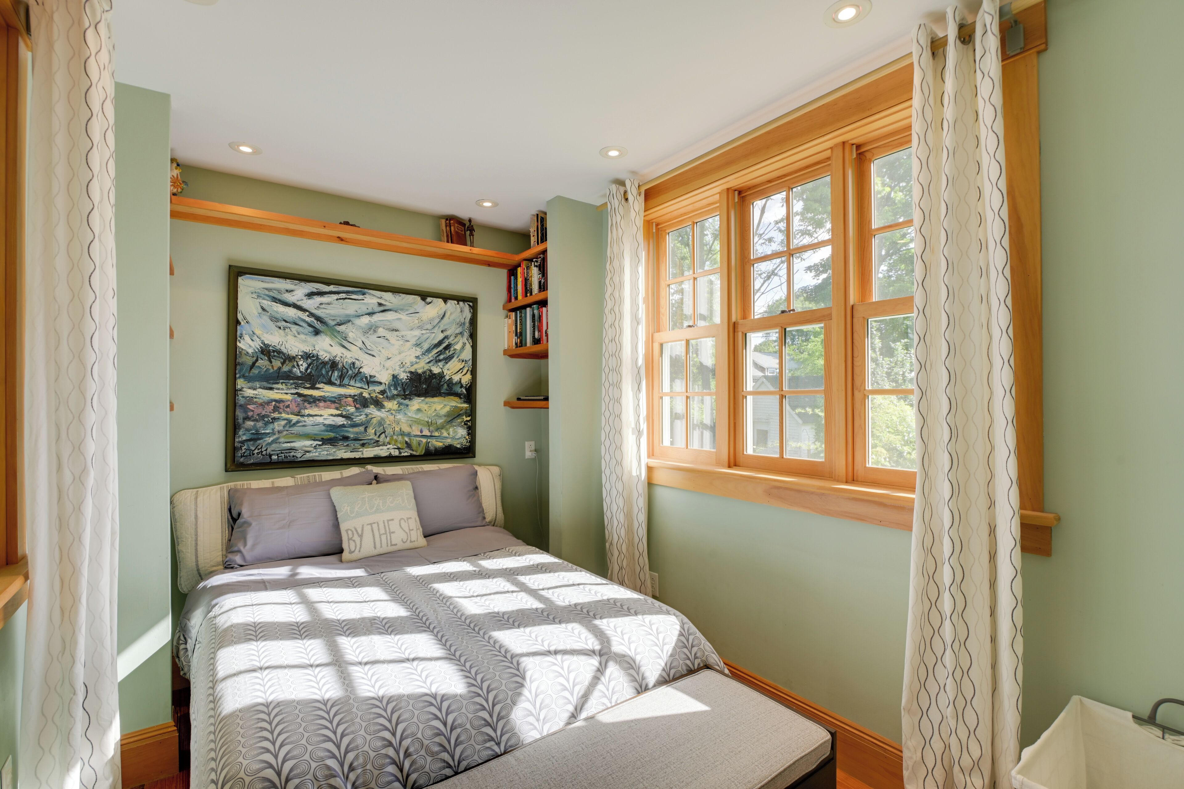 Un dormitorio con cama, un cuadro grande, una ventana con cortinas y una estantería.