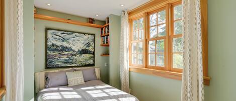 Un dormitorio con cama, un cuadro grande, una ventana con cortinas y una estantería.