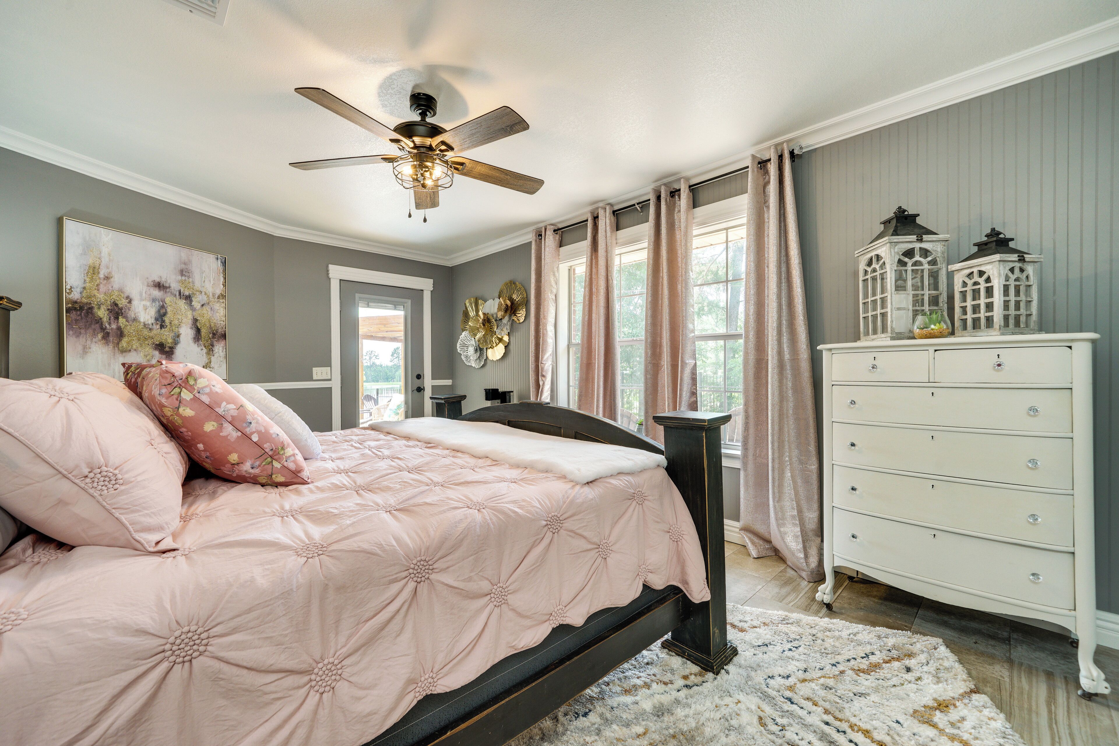A bedroom with a bed, a dresser, a ceiling fan, and a window with curtains.