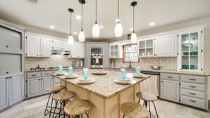A spacious kitchen with white cabinets, a granite island with bar stools, and pendant lighting. - Broken Bow Vacation Rental w/ Pool & Hot Tub! (Broken Bow)