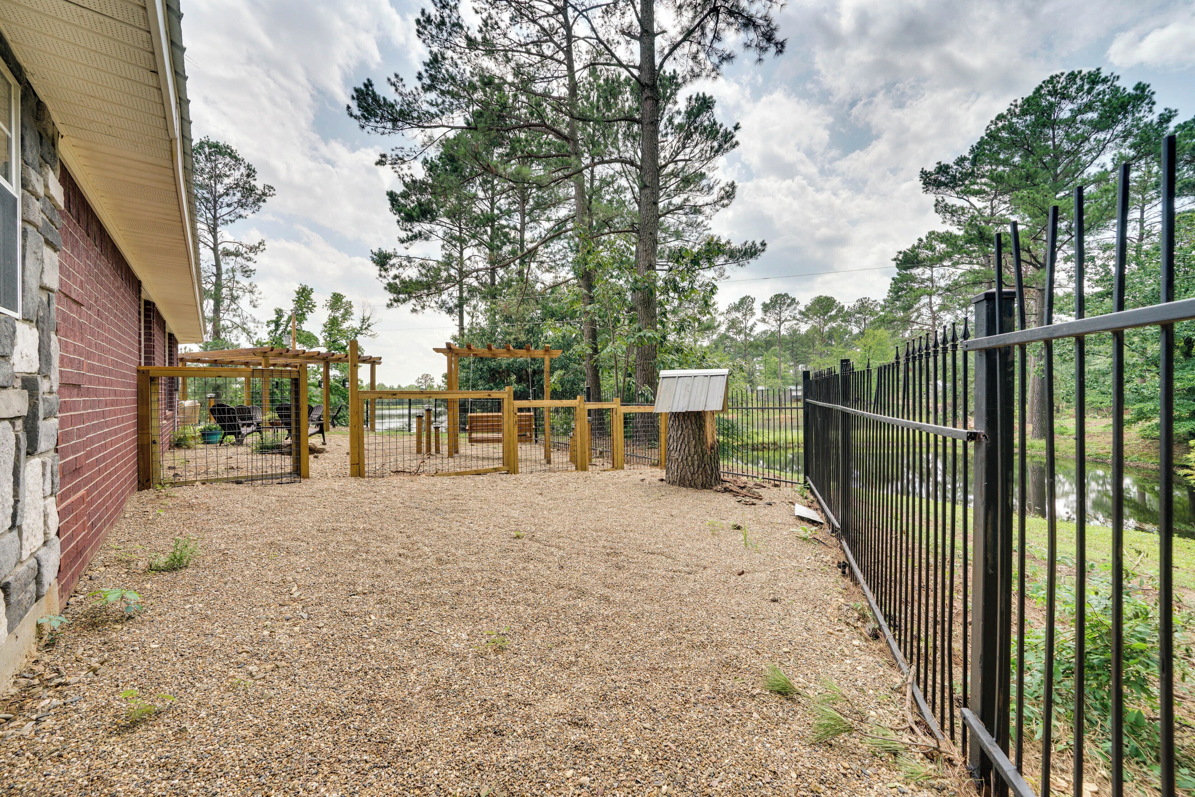 A gravel patio with a wooden pergola, a fenced area, and a building with a brick exterior.