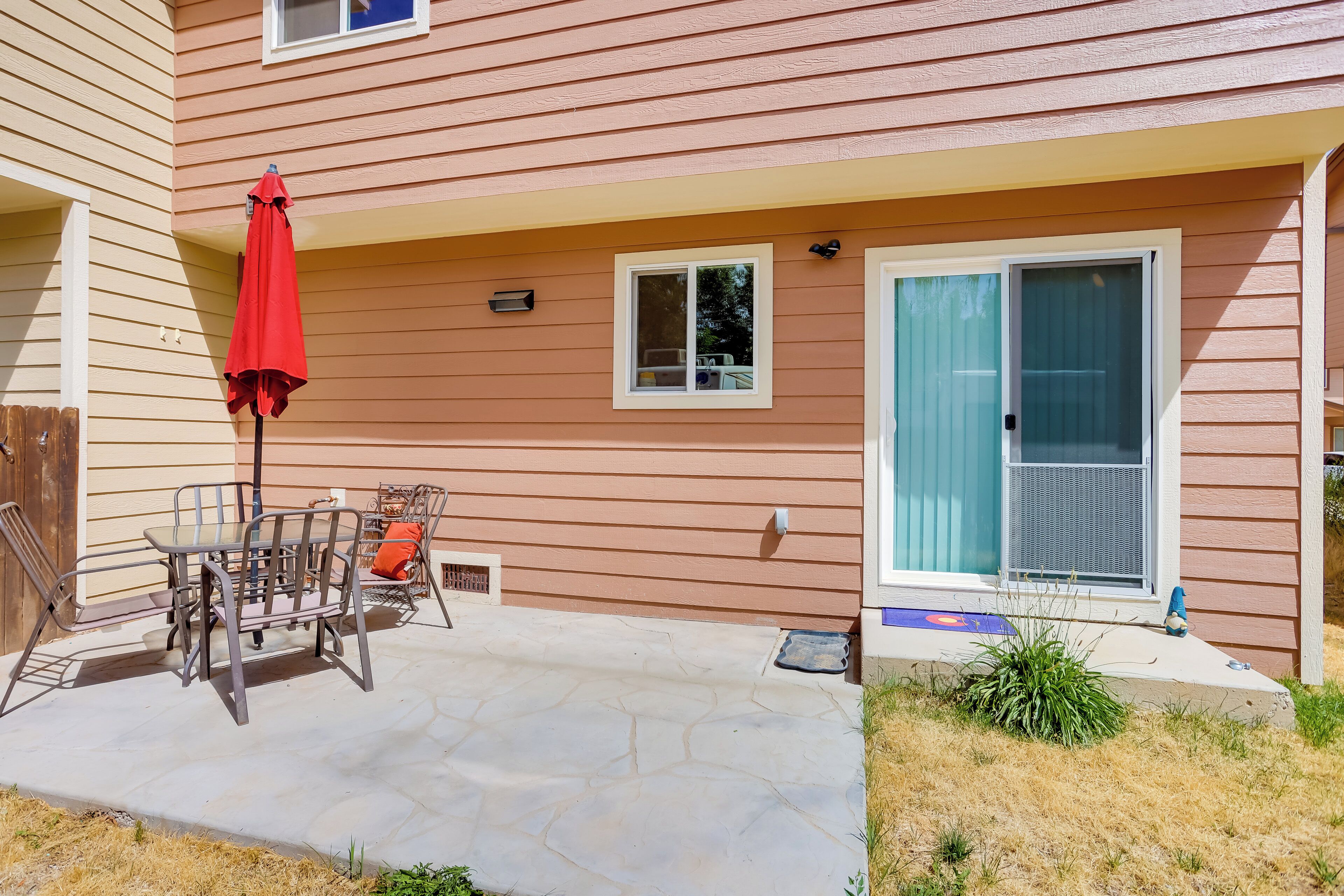 A patio with a table and chairs, a red umbrella, and a sliding glass door.