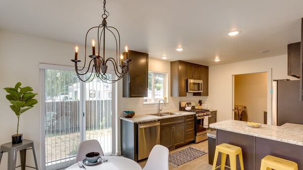 A modern kitchen with a central island, stainless steel appliances, and a dining area with white chairs and a table. - Dolores Townhome w/ Mountain Views: Near River! (Dolores)
