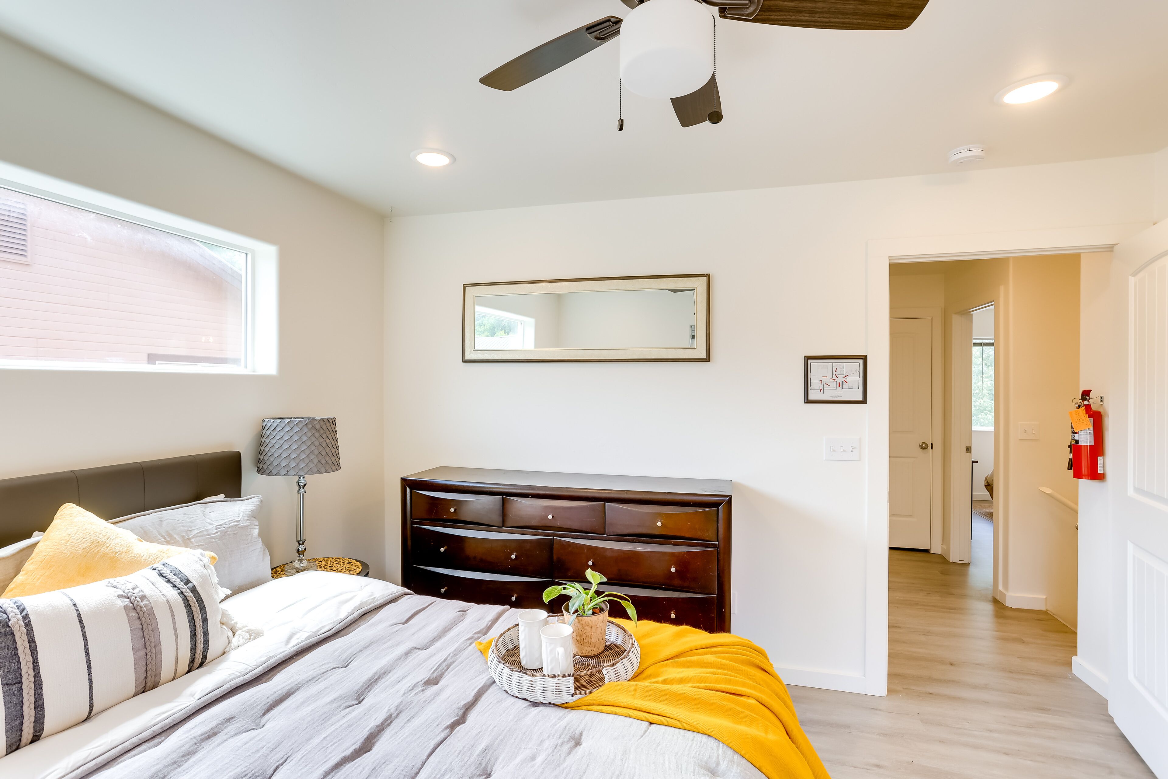 A bedroom with a bed, a dresser, a ceiling fan, a window, and a hallway.
