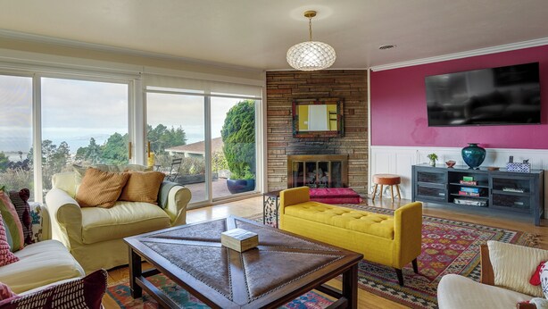 A living room with a fireplace, a television mounted on the wall, and a large window offering a view of the outdoors. - Stunning Bay-view Home in Kensington! (Berkeley)