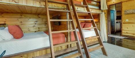 A wooden cabin with bunk beds, a ladder, and a visible kitchen area.