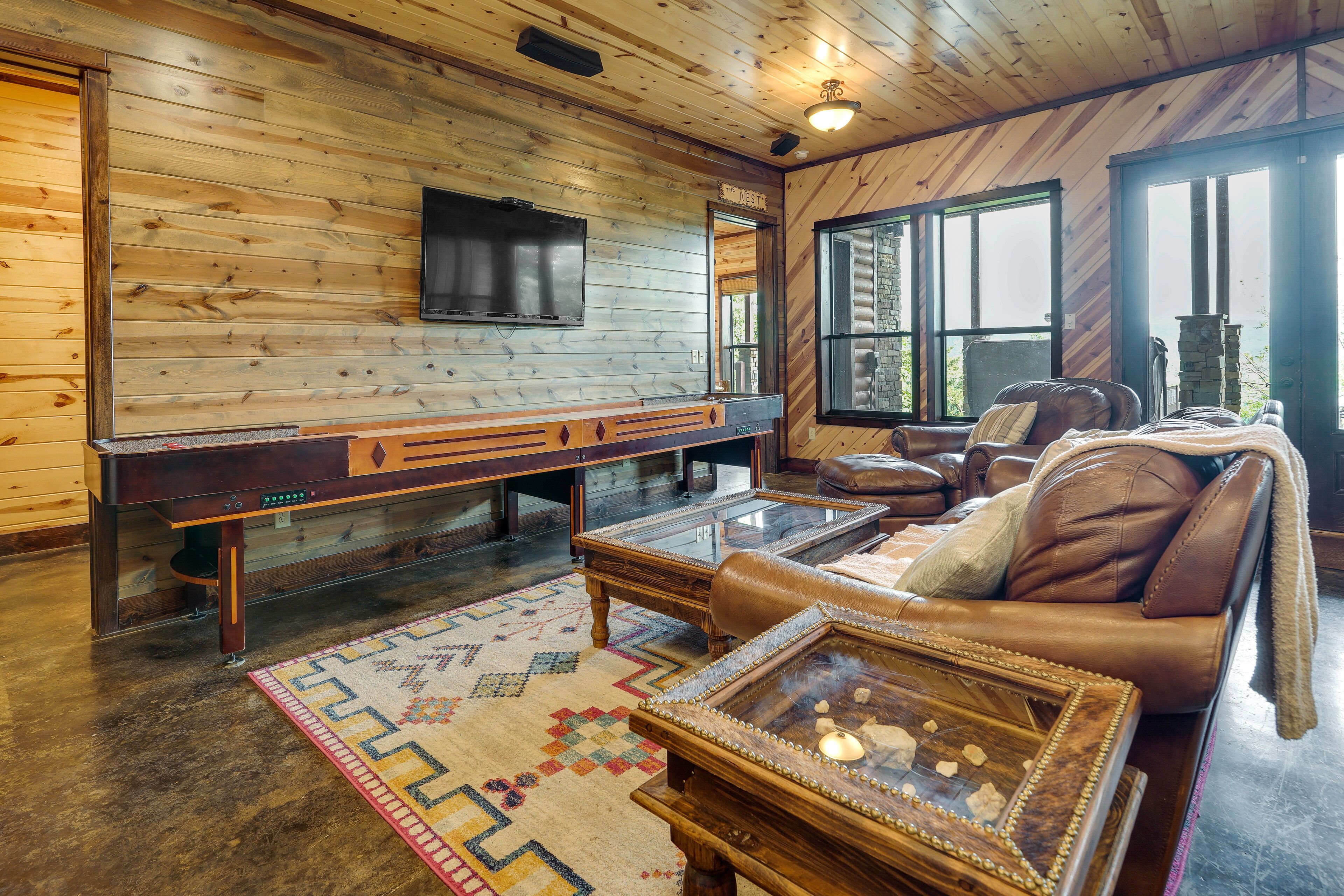Een gezellig chaletinterieur met houten inrichting, een biljarttafel, lederen zitplaatsen en een groot raam.