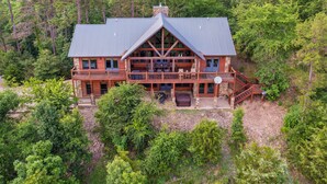 A large log cabin with a prominent gable roof, multiple decks, and a stone chimney. - Broken Bow Cabin w/ Game Room & Private Hot Tub! (Broken Bow)