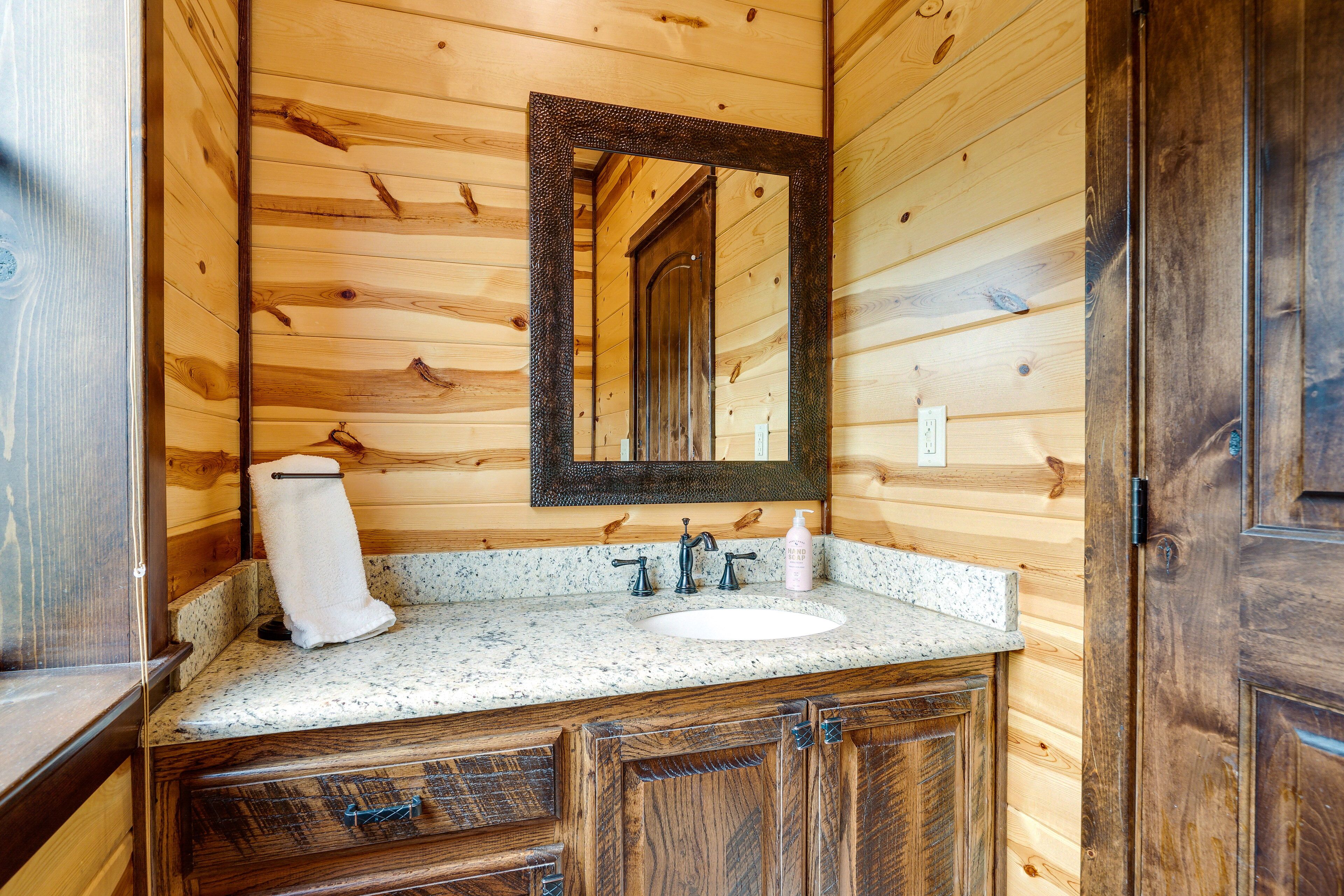 A wooden cabin bathroom with a granite countertop, a sink, a mirror, and wooden cabinets.
