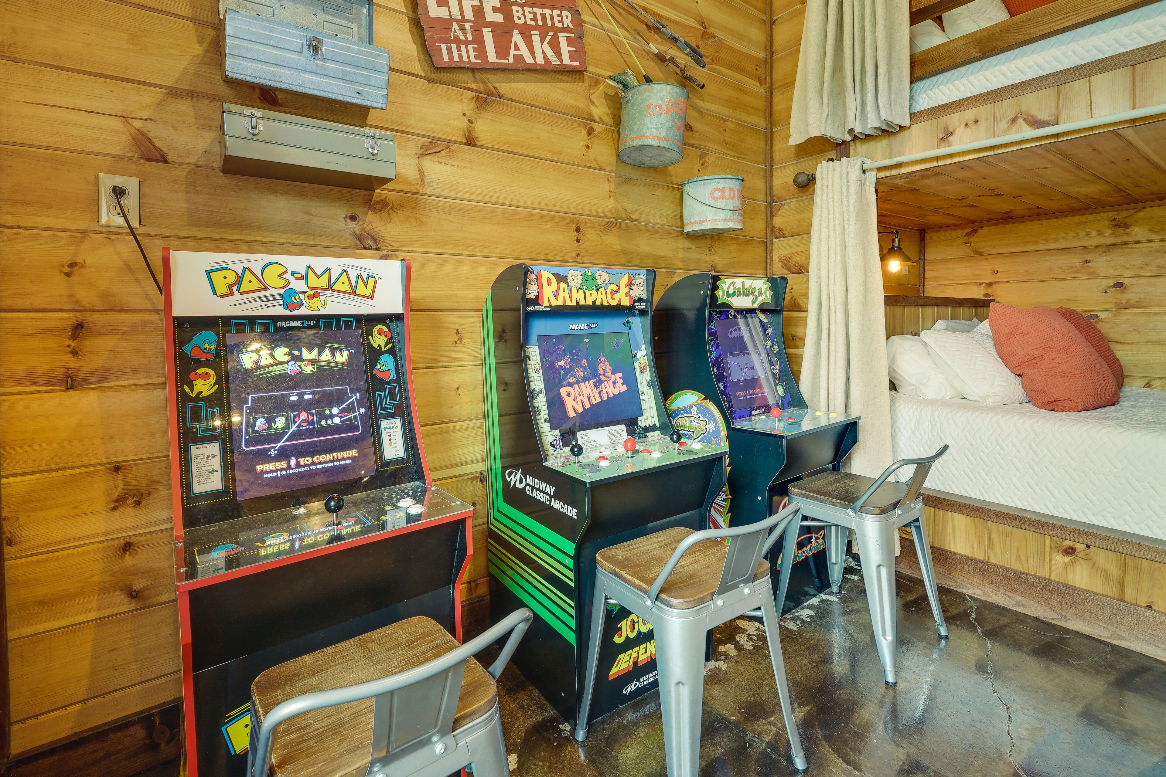 Una habitación con paredes de madera, una cama litera y máquinas de videojuegos, incluyendo Pac-Man y Rampage.