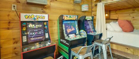 Una habitación con paredes de madera, una cama litera y máquinas de videojuegos, incluyendo Pac-Man y Rampage.