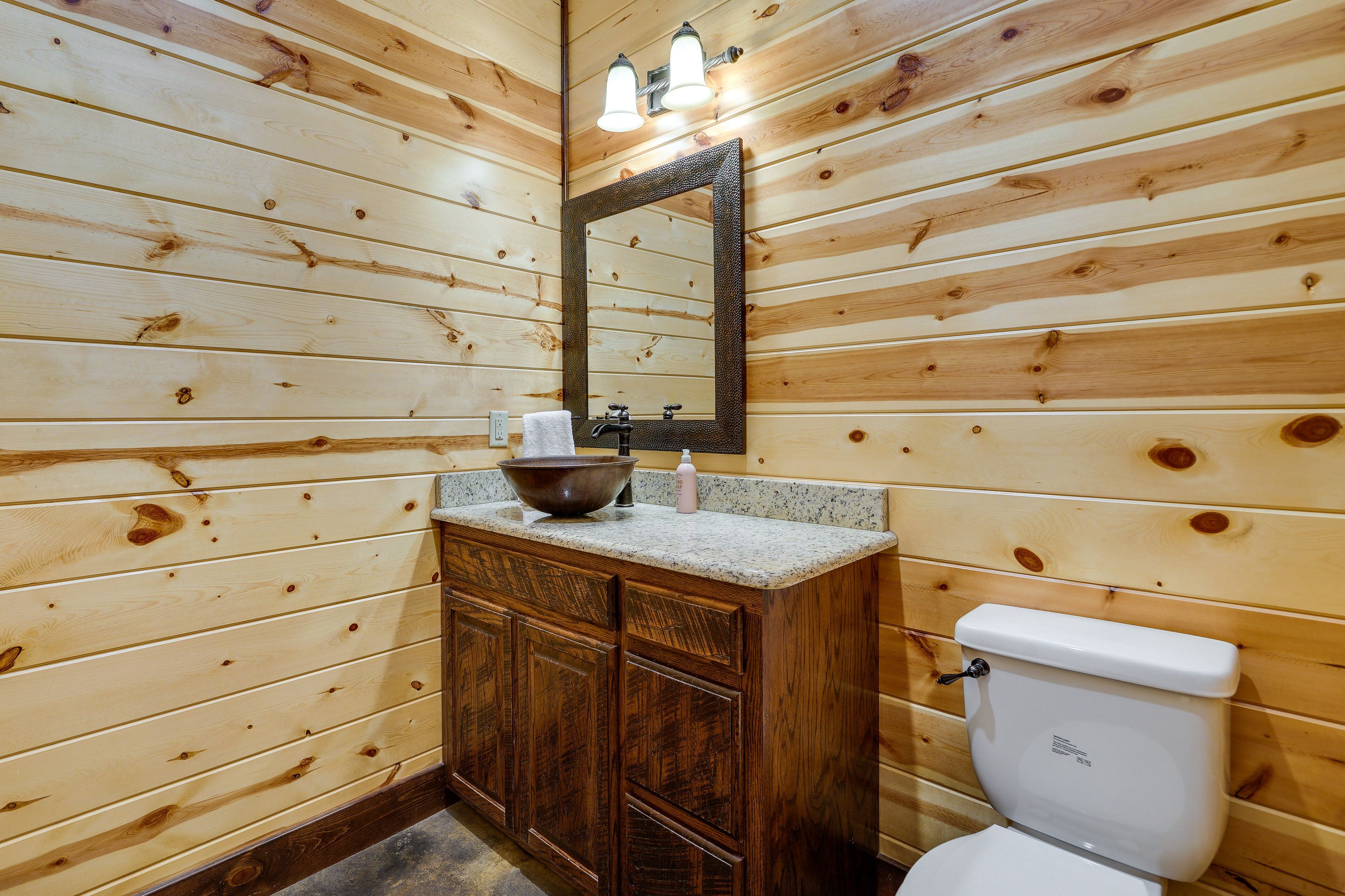 A wooden cabin bathroom with a wooden vanity, a large mirror, a sink, and a toilet.