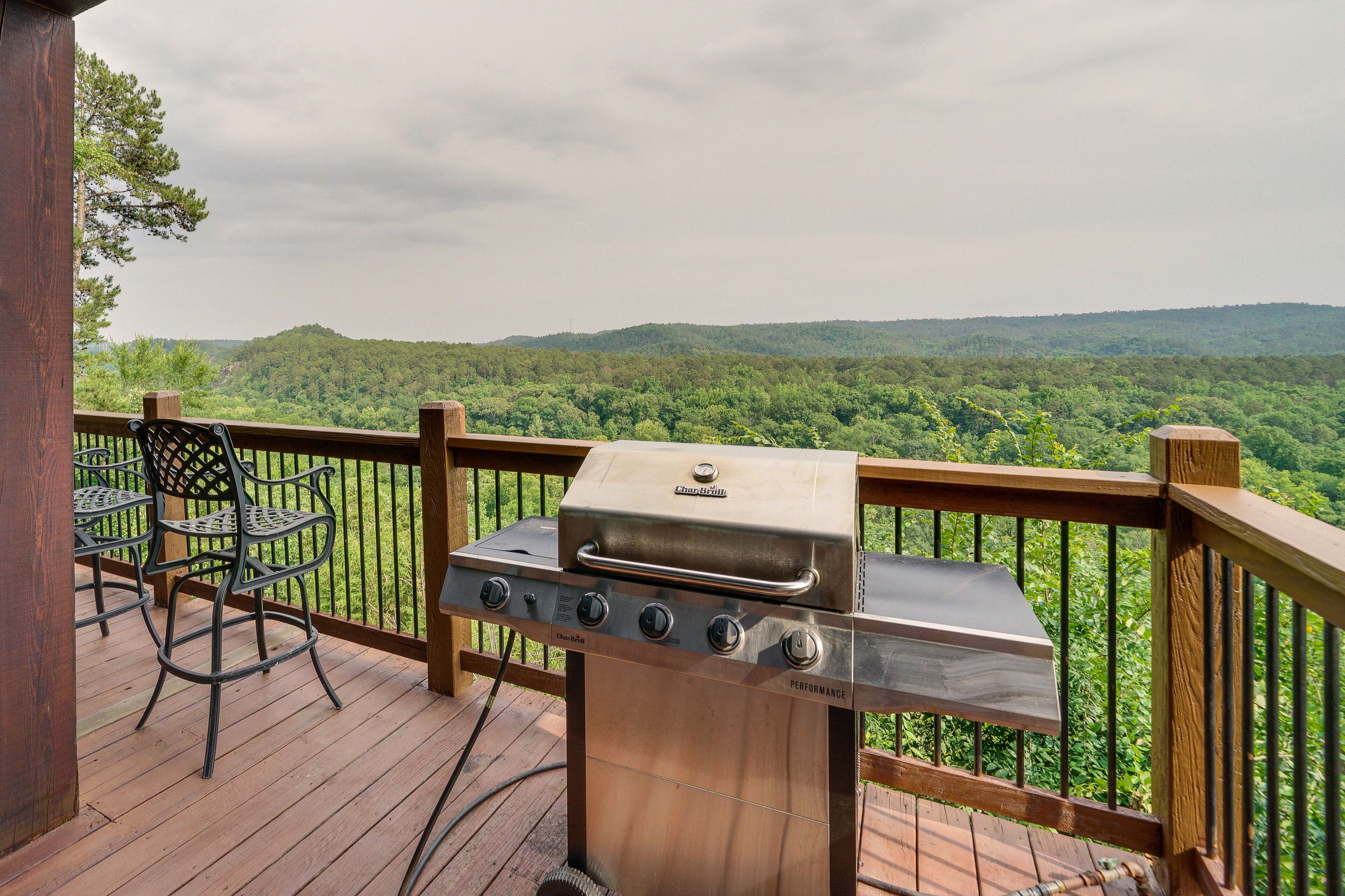 A barbecue grill on a wooden deck with a view of a forested landscape.