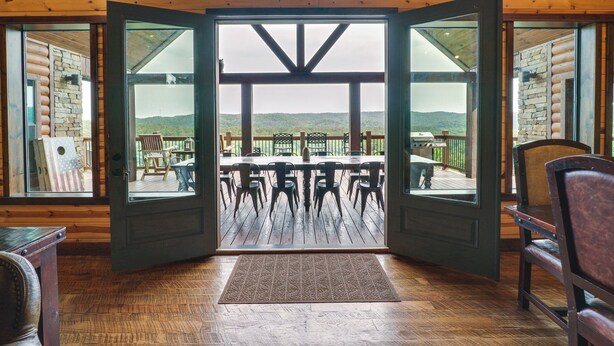 A wooden interior with a large open door leading to an outdoor patio with tables and chairs. - Broken Bow Cabin w/ Game Room & Private Hot Tub! (Broken Bow)