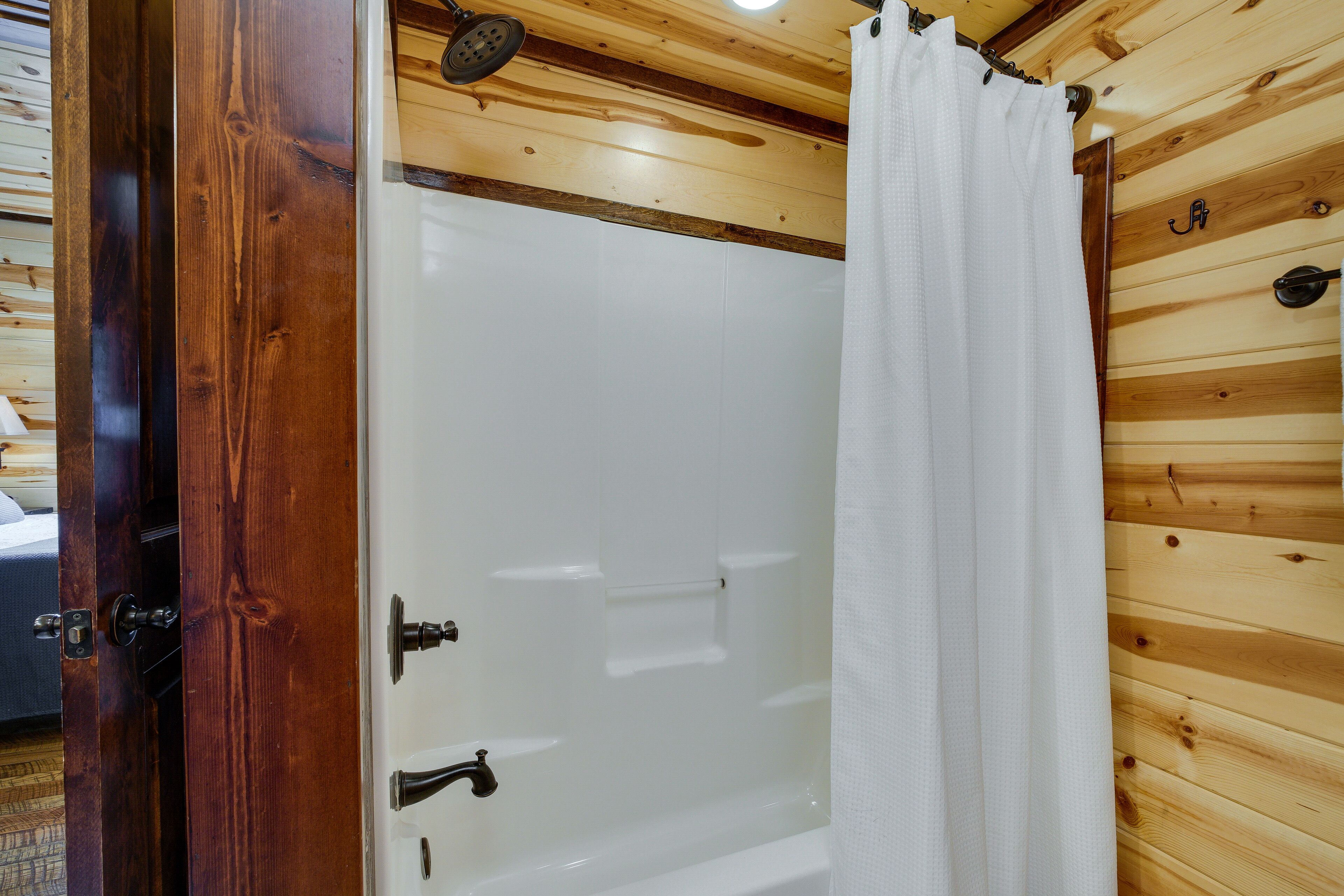 A wooden-paneled bathroom with a white bathtub, a shower curtain, and a visible door handle.